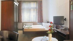 Habitación de hotel con cama, escritorio con televisor, silla, mesa con florero y ventana con cortinas.
