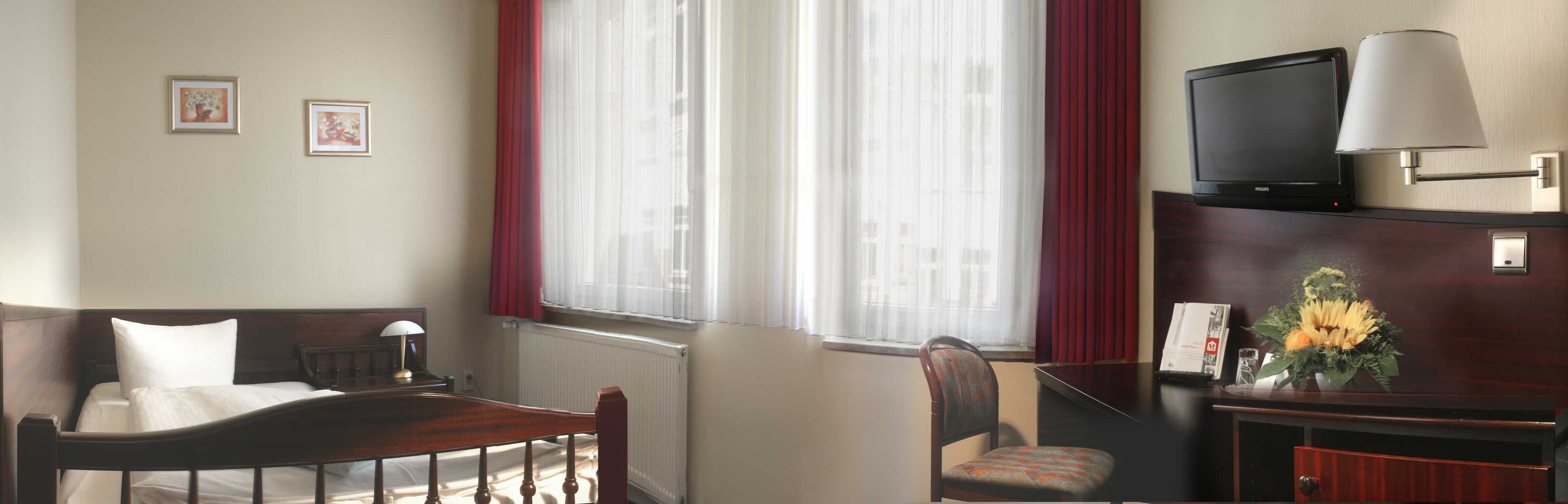 A hotel room with a bed, a desk, a chair, a television, and a window with curtains.