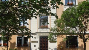 Un edificio con un cartel que indica 'MARTHA-HAUF' en la entrada, que presenta un estilo arquitectónico tradicional con una puerta central, ventanas con macetas de flores y una acera pavimentada.