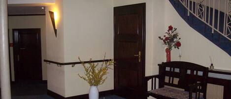 A hallway with a white vase, a wooden bench, a staircase with white railings, and a dark door.