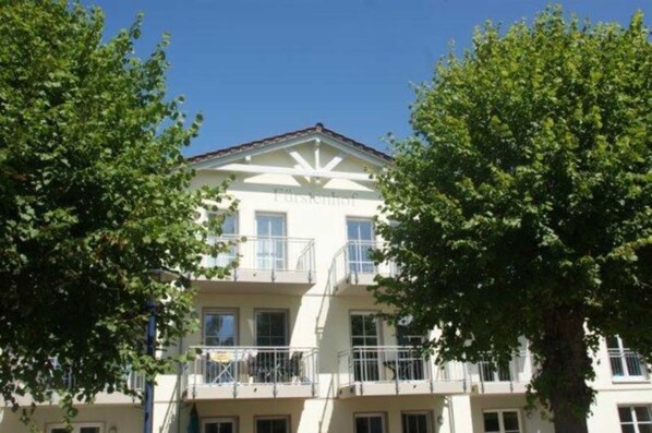 Un edificio de varios pisos con balcones, rodeado de árboles.