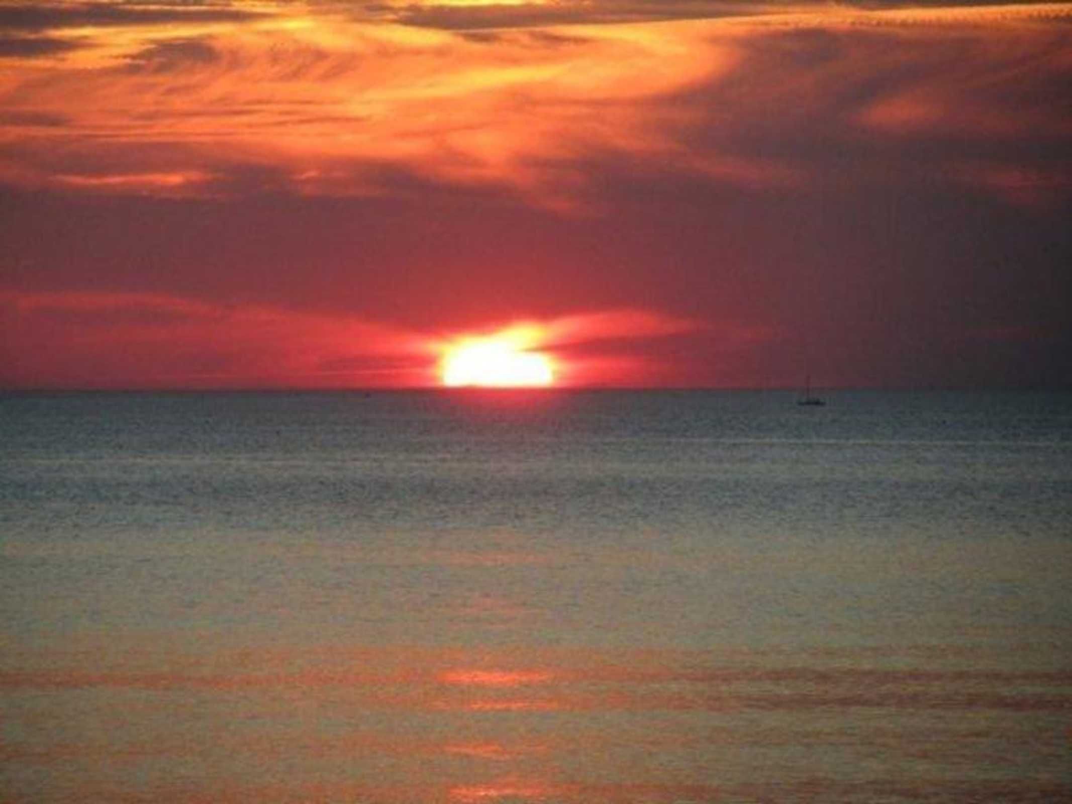 Ein Sonnenuntergang über ruhigem Meer, ein Boot in der Ferne.