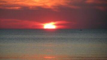 Ein Sonnenuntergang über ruhigem Meer, ein Boot in der Ferne.