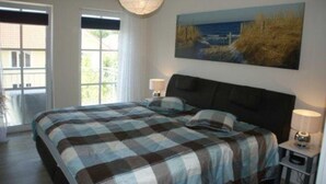 Ein Schlafzimmer mit einem großen Bett, einem Gemälde einer Küstenlandschaft und einem Fenster mit Vorhängen.