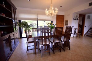 Un comedor espacioso con una araña, sillas de madera, una mesa y una planta en maceta.