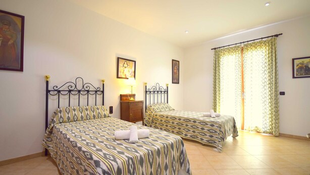 Habitación de hotel con dos camas, una mesita de noche, una lámpara y una ventana con cortinas.