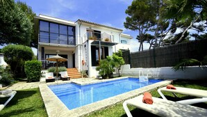 Una casa moderna con piscina, un patio cubierto y un jardín cuidado.