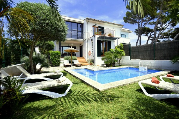 A modern two-story house with a swimming pool, outdoor seating, and lush greenery.