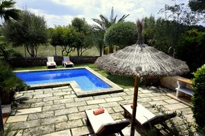 A swimming pool with a stone border, surrounded by lounge chairs and a thatched umbrella.