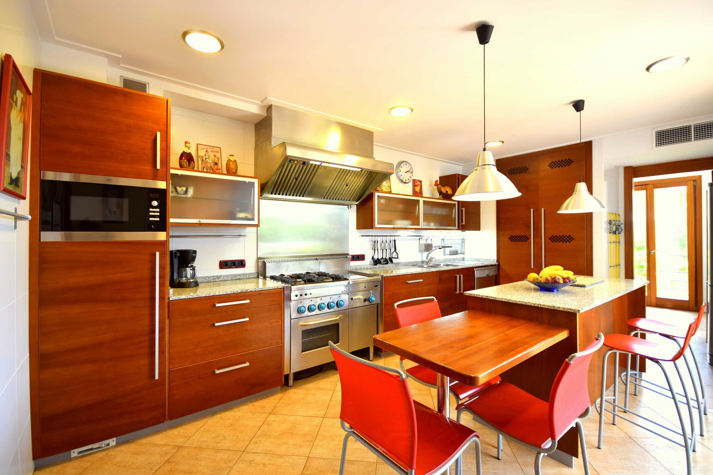 Cocina moderna con alacenas de madera, estufa a gas, microondas y un comedor con sillas rojas.