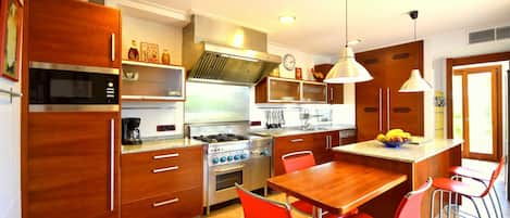 Cocina moderna con alacenas de madera, estufa a gas, microondas y un comedor con sillas rojas.