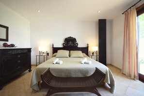Una habitación de hotel con una cama grande, dos mesitas de noche con lámparas, un aparador de madera y un banco.