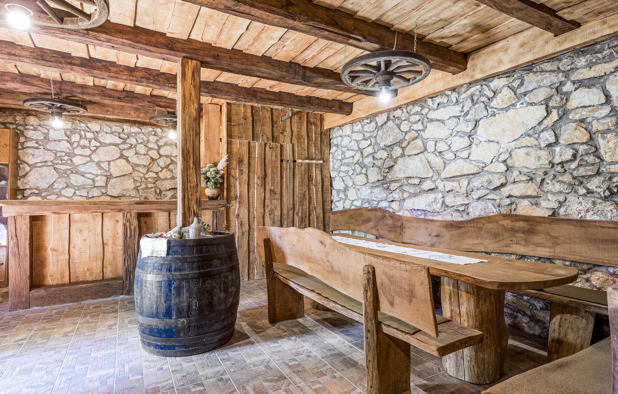 A rustic interior with a stone wall, wooden beams, a barrel, and a bench.