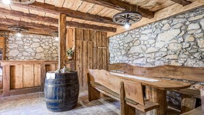 Un interno rustico con parete in pietra, travi in legno, una botte e una panca.