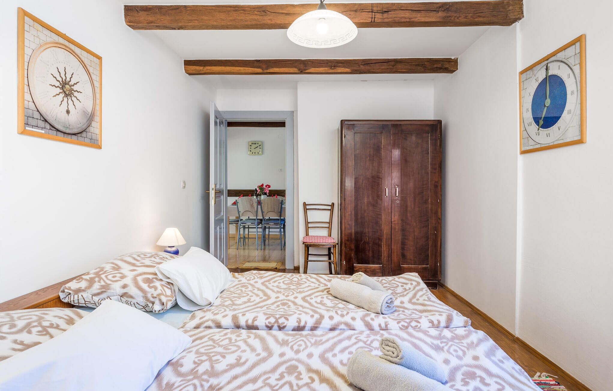 A bedroom with a bed, a chair, a wooden door, and a hallway leading to a dining area.