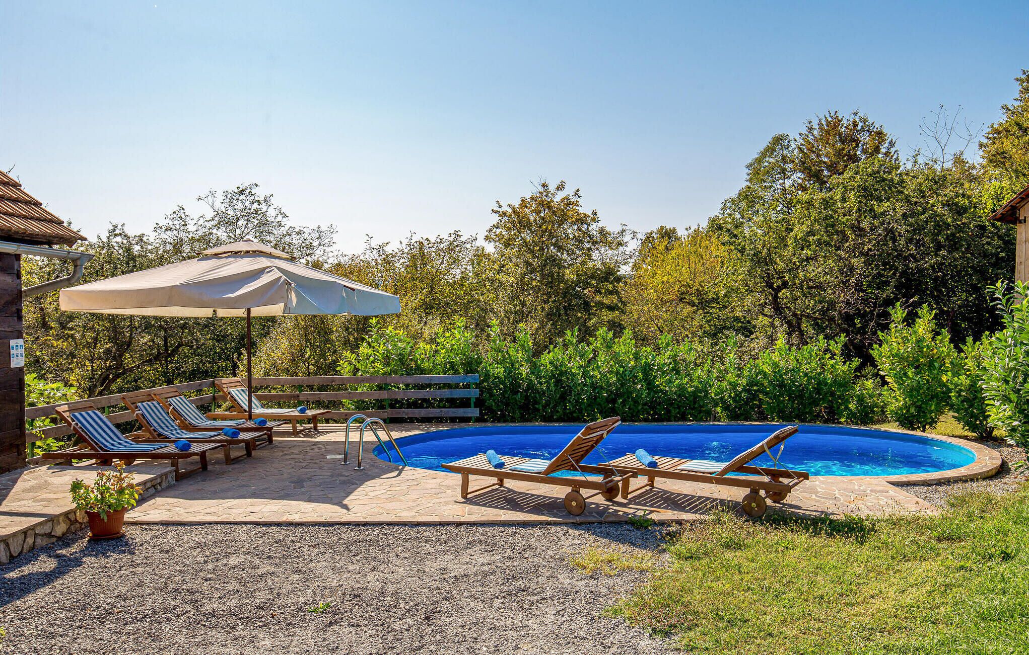 A pool area with lounge chairs and a covered umbrella, surrounded by greenery.