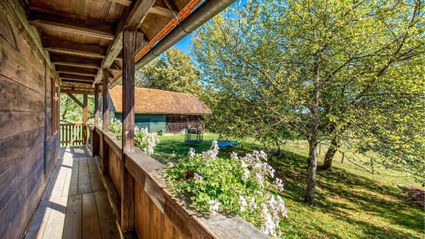Un balcone in legno con vista su un edificio rustico e un cortile alberato.
