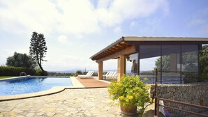 Una piscina de piedra con una terraza de madera, un espacio de estar cubierto y vistas al paisaje.