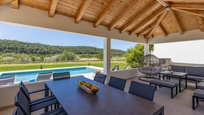 Un espacio al aire libre cubierto con vista a la piscina, un sillón colgante y una mesa con fruteros.
