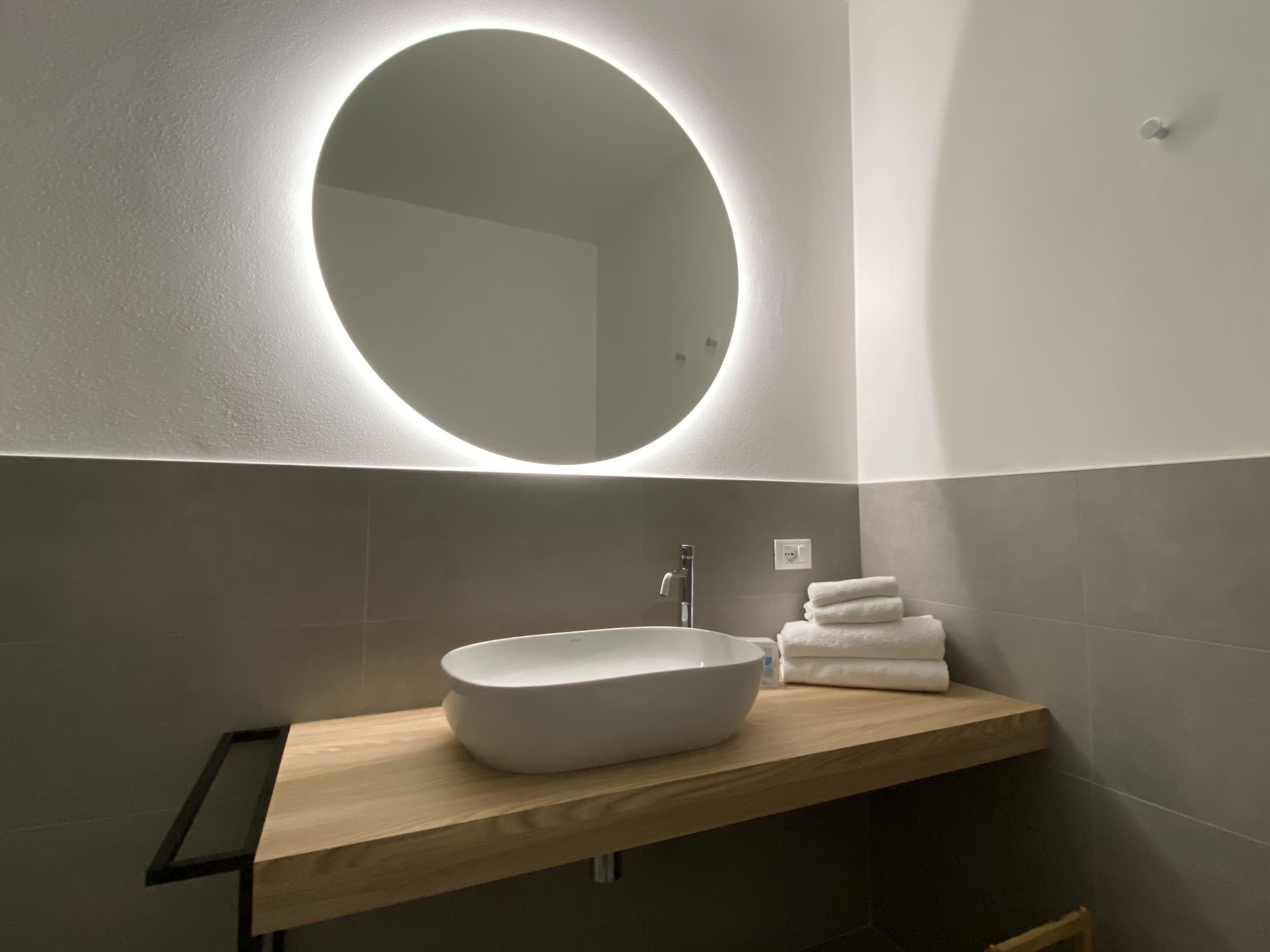 Un baño moderno con un espejo redondo, un tocador de madera y un lavabo blanco.