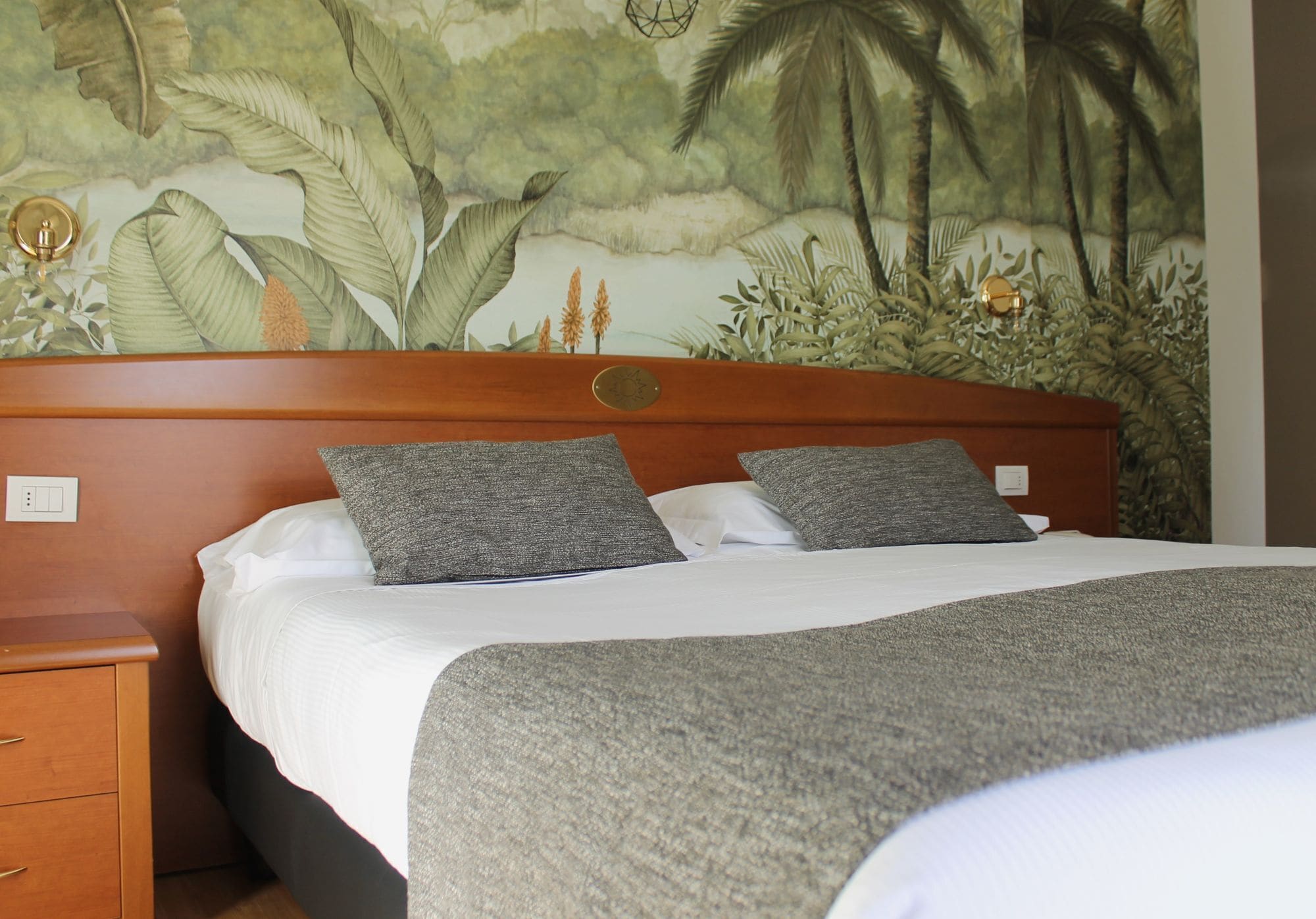 Een hotelkamer met een bed, nachtkastje, houten hoofdeinde en een muurschildering.