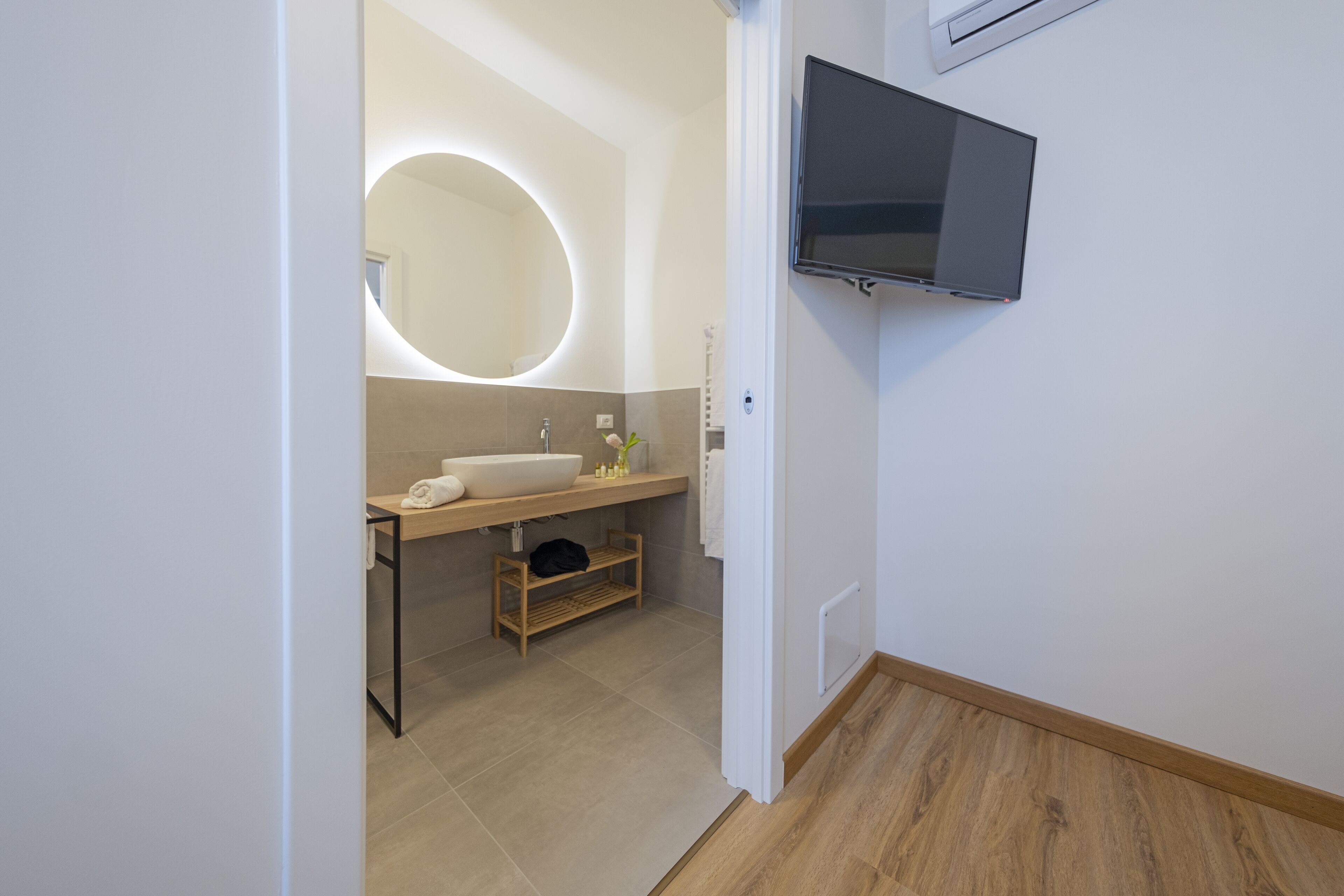 Une salle de bain moderne avec un miroir rond, un lavabo et un téléviseur fixé au mur.