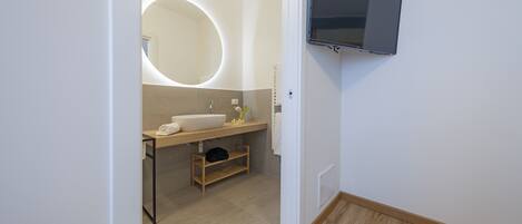 Une salle de bain moderne avec un miroir rond, un lavabo et un téléviseur fixé au mur.