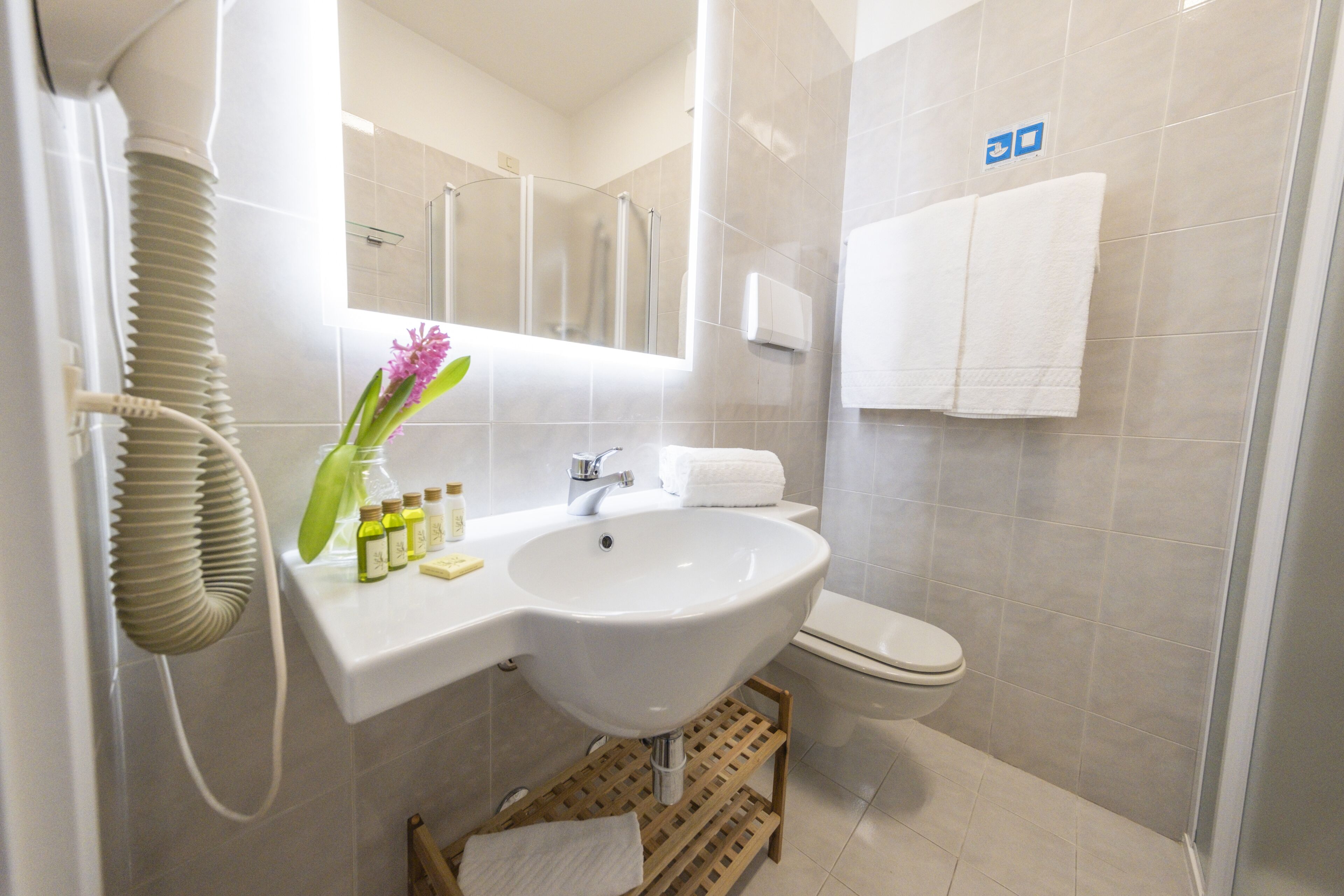 A modern bathroom with a white sink, mirror, and toilet. There is a shower area with a glass door, and a towel rack with two towels.