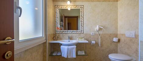 A bathroom with a white sink, a mirror with a decorative frame, a toilet, and a glass shelf with towels.