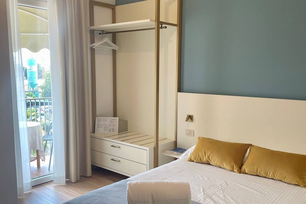 Une chambre d’hôtel avec un lit, une table de chevet, une armoire et une fenêtre avec des rideaux.