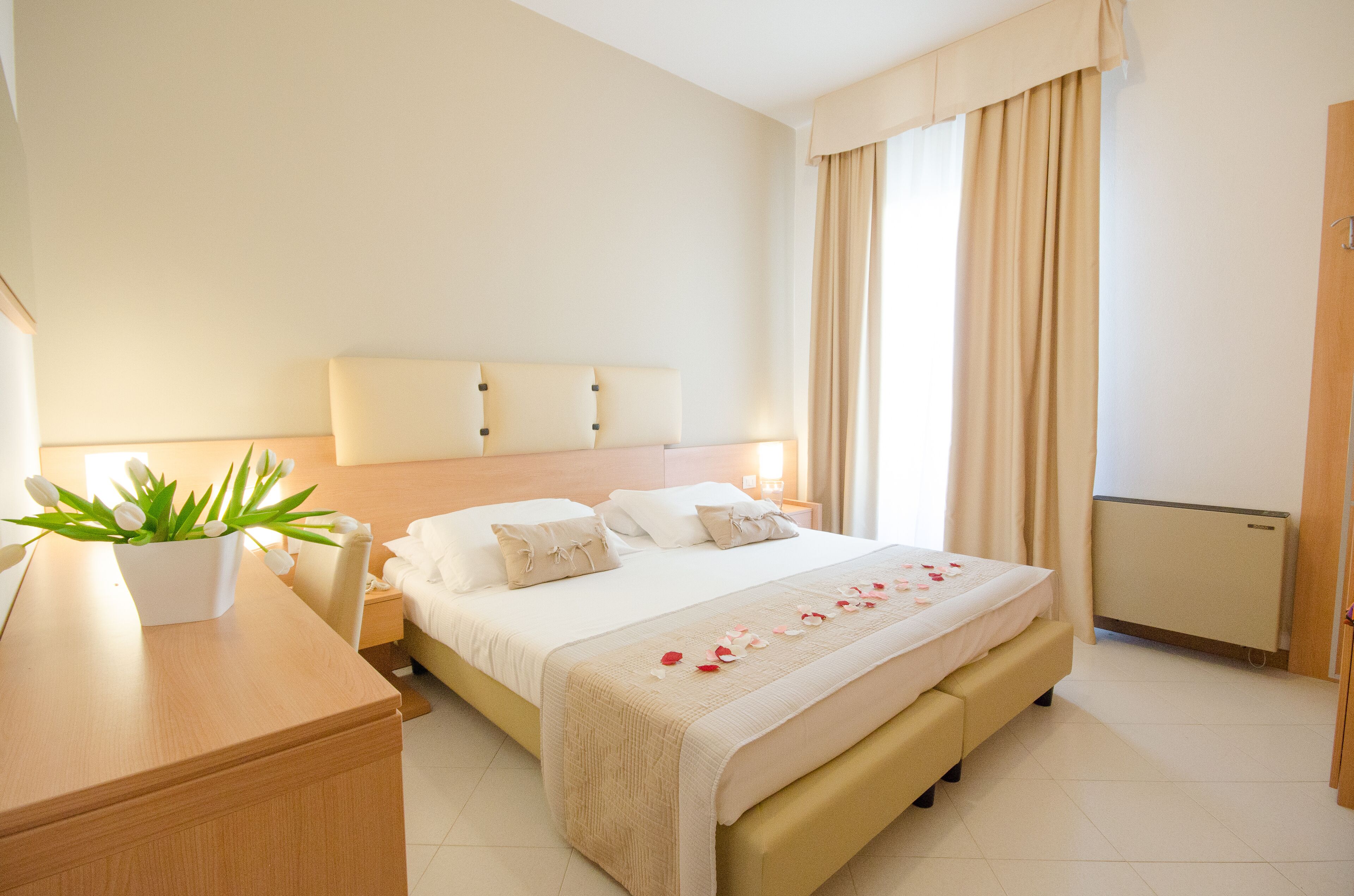 A hotel room with a bed, bedside table, lamp, and a potted plant.
