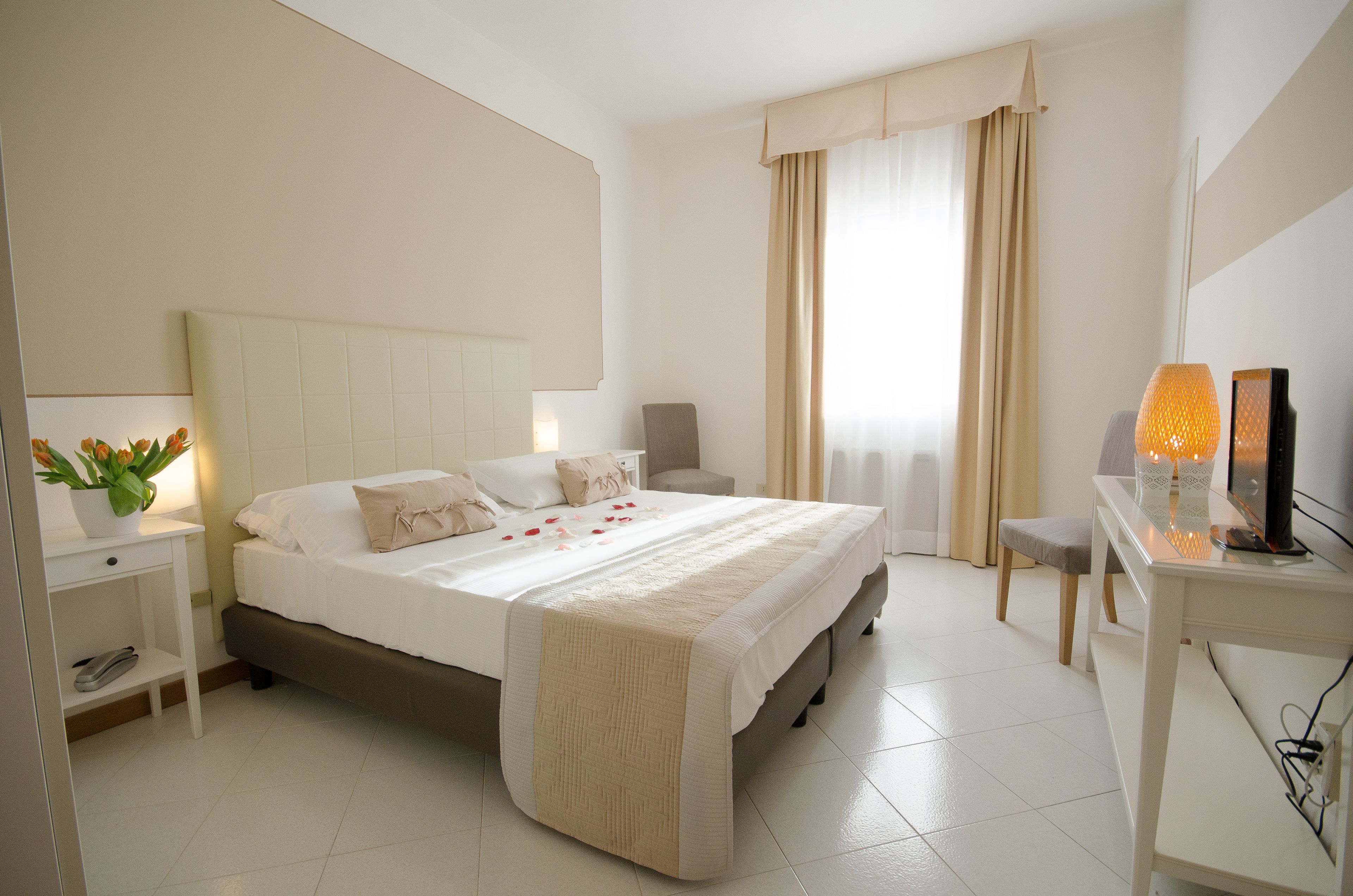 A neatly arranged bedroom with a bed, bedside table, chair, and a desk with a lamp.