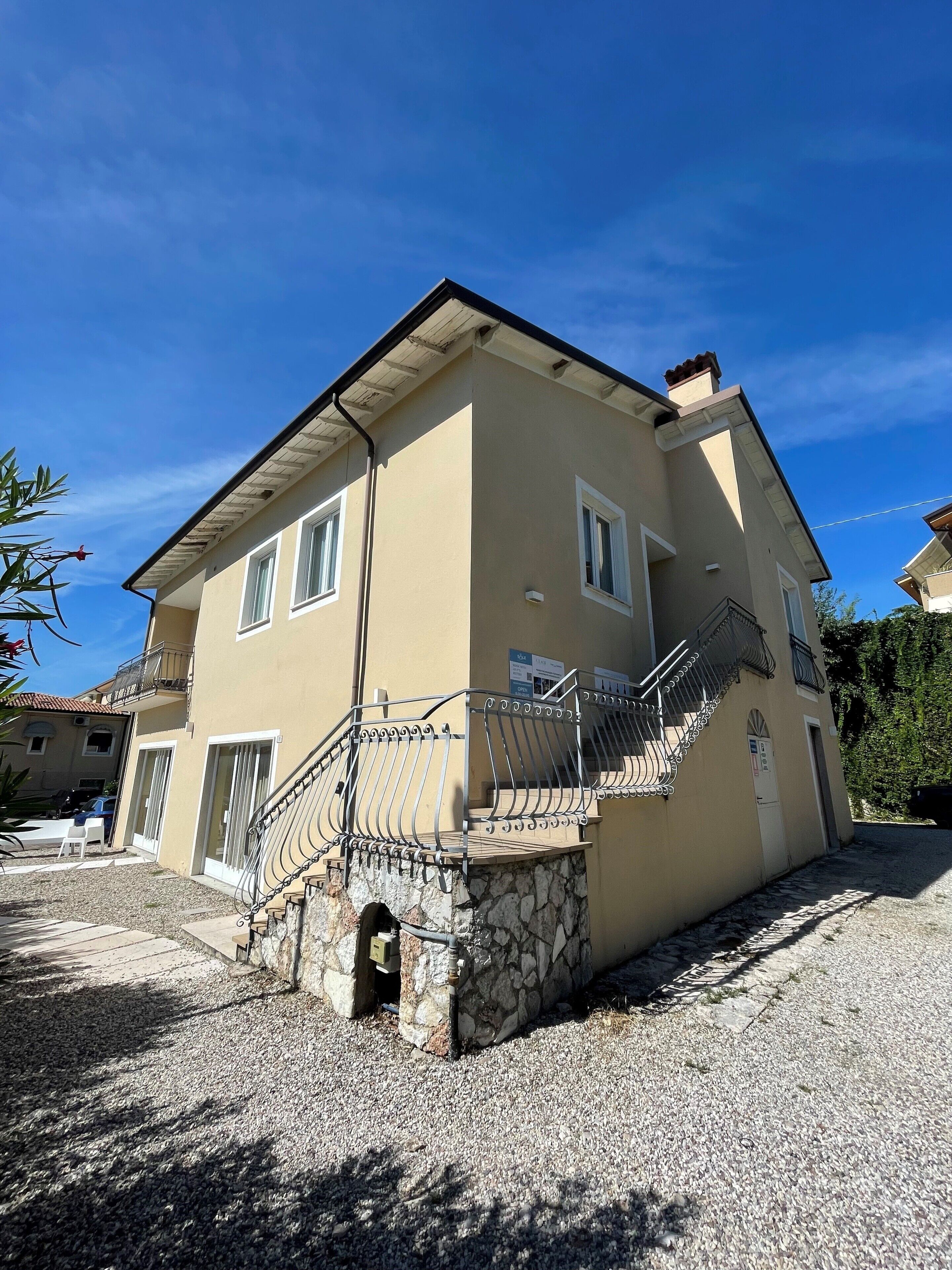 A two-story house with a stone foundation, a metal staircase with a balustrade, and a clear blue sky.