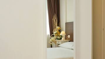 Habitación de hotel con un espejo grande, una cama, una mesita de noche con lámpara y una ventana con cortinas.
