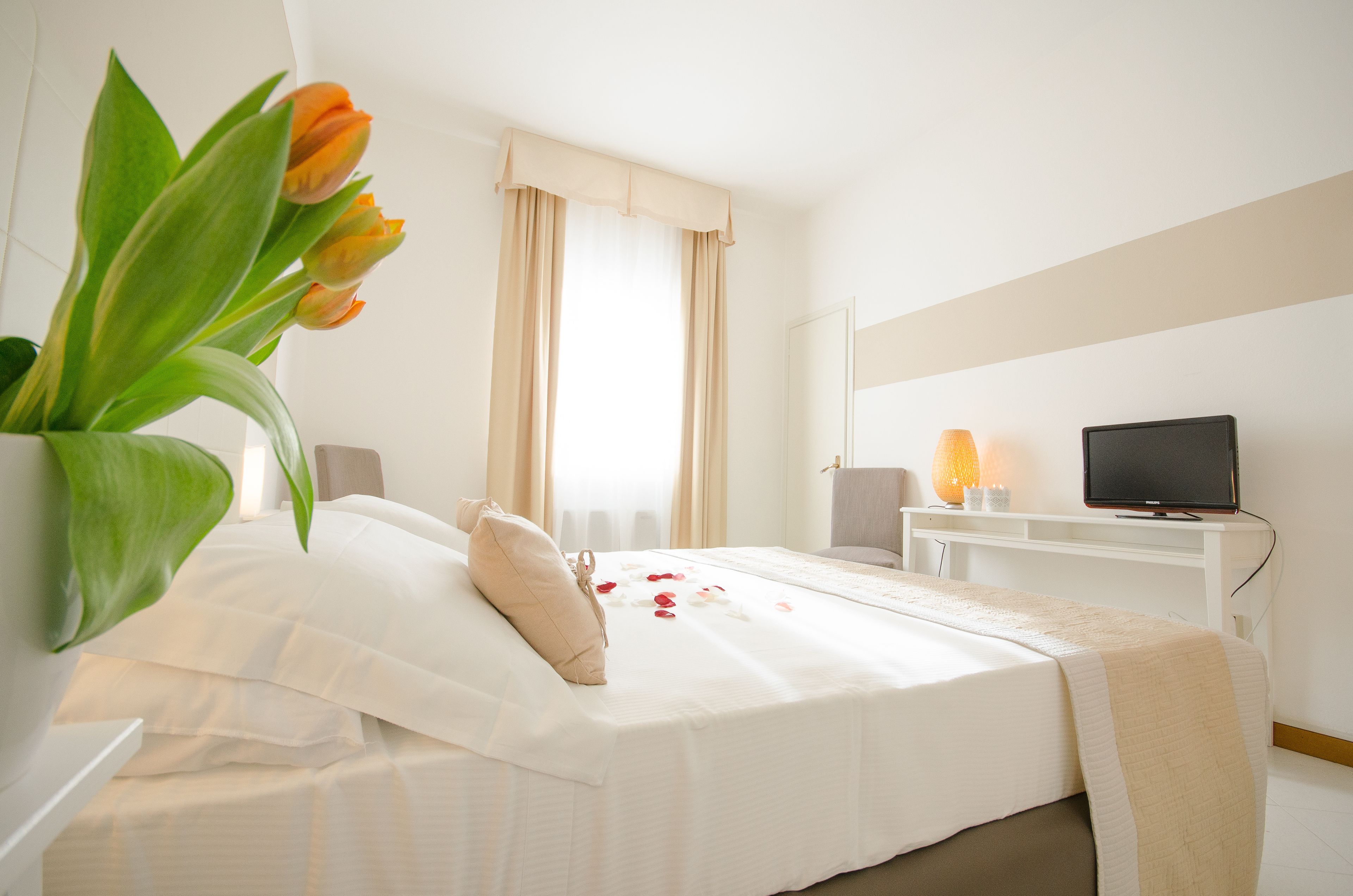 Una habitación de hotel con cama, televisión, escritorio con lámpara y ventana con cortinas.