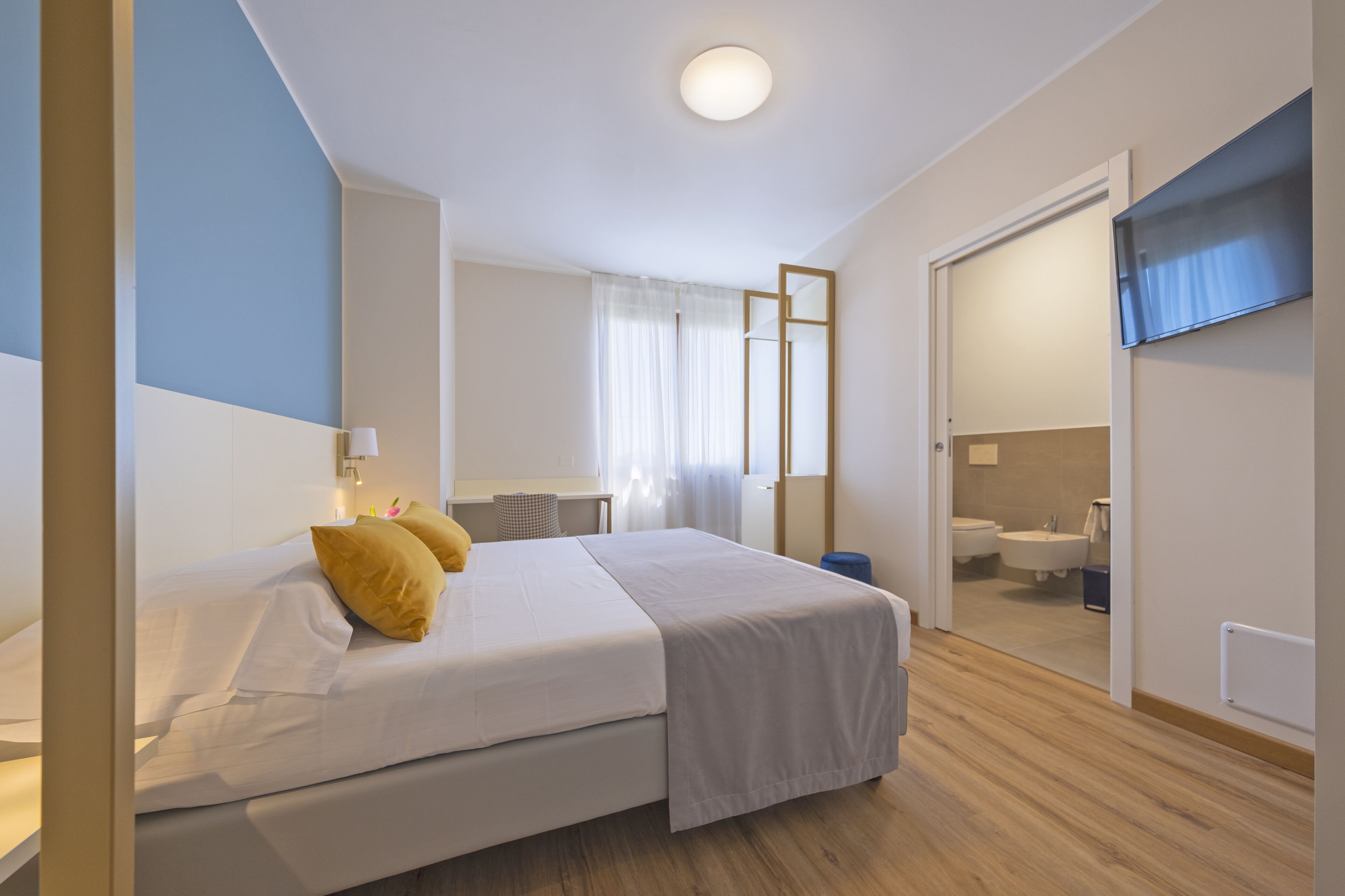 Et hotelværelse med seng, fjernsyn, badeværelse med håndvask og toilet samt et spejl.