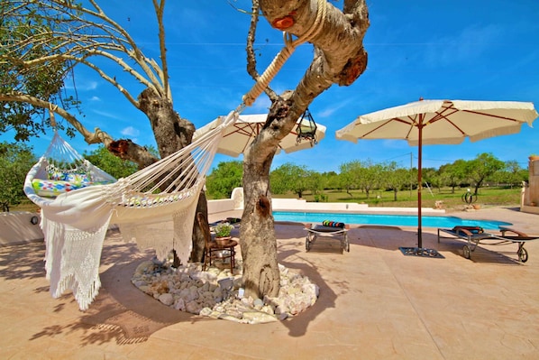A hammock, outdoor seating, a pool, and a clear sky.