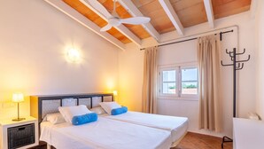 Une chambre d’hôtel comprenant un lit, deux lampes de chevet, un ventilateur de plafond, une fenêtre avec des rideaux et un porte-manteau.