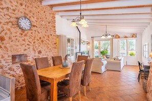 A dining area with a wooden table and chairs, a clock on the wall, and a view of the outdoors through a doorway. - 44250 Finca Es Estador (Manacor)