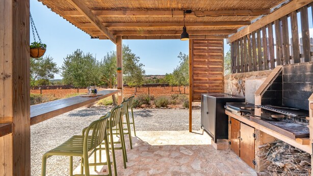 Une terrasse extérieure dotée d’une pergola en bois, d’un barbecue et d’un espace détente avec des chaises.