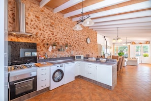 A modern kitchen with a stone wall, built-in appliances, and a dining area with a view. - 44250 Finca Es Estador (Manacor)