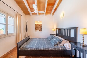 A bedroom with a bed, a desk, a lamp, a ceiling fan, a window, and a wall-mounted light fixture.
