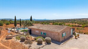 A rustic stone building with a tiled roof, a swimming pool, and a clear view of the surrounding countryside.