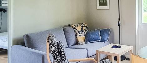 Ein Wohnzimmer mit grauem Sofa, gemusterten Sesseln, einem kleinen Tisch und einer Stehlampe.