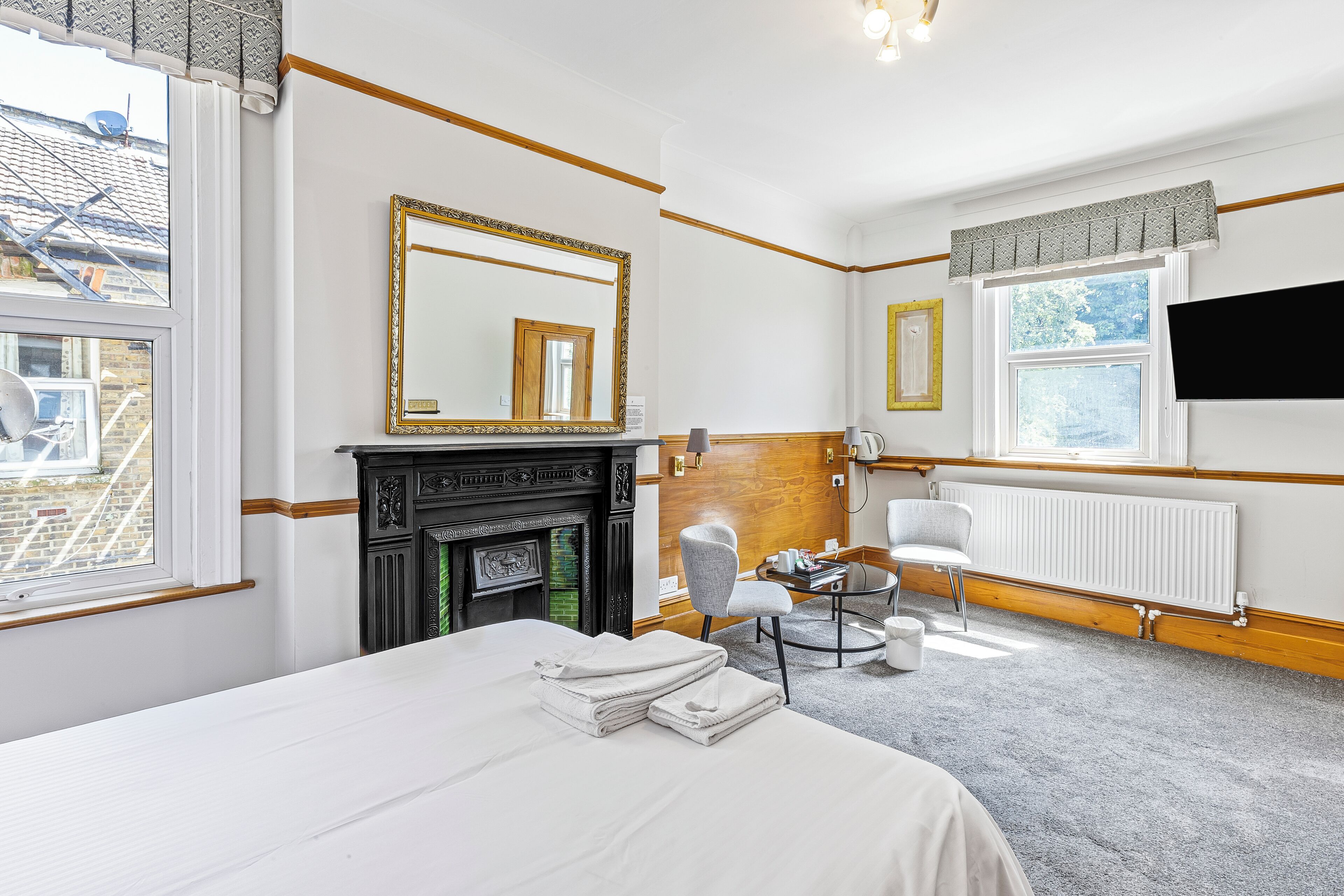 A hotel room with a bed, a fireplace, a mirror, a chair, and a TV.