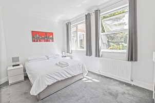 Un dormitorio con cama, mesita de noche, ventana con cortinas y radiador.