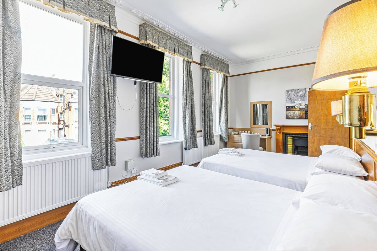 A hotel room with two beds, a TV mounted on the wall, a fireplace, and a large window with curtains.