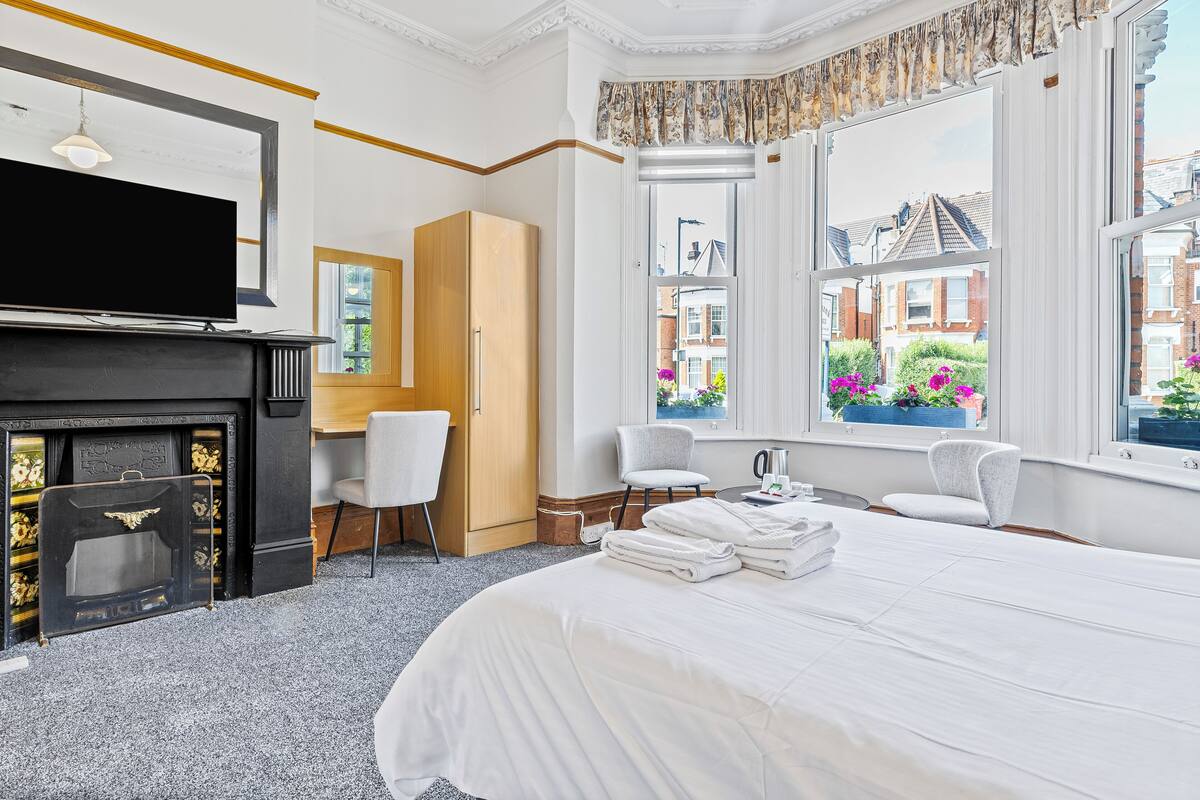 A hotel room with a bed, a TV, a fireplace, a desk, and a view of the outside.