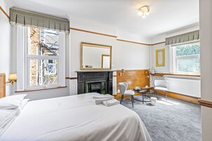 Habitación de hotel con una cama grande, chimenea, espejo, ventana con vistas y una silla.