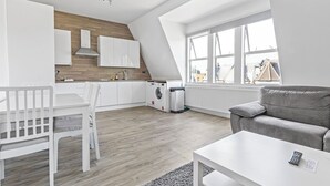 Un appartamento moderno con cucina, zona pranzo e soggiorno. Dispone di un soffitto a soppalco, ampie finestre e un divano grigio.